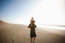 Батько носить сина на плечах уздовж пляжу — стокове фото