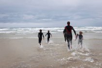 Family running in to the sea in wetsuits — Stock Photo