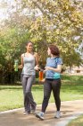 Young women out walking wearing sports clothing carrying water bottles talking — Stock Photo