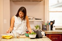 Mujer joven haciendo batido verde en la cocina - foto de stock