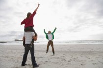 Young man carrying girl on shoulders on beach — Stock Photo