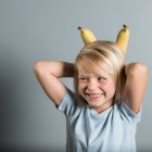Retrato de niño con las manos detrás de la cabeza sosteniendo plátanos - foto de stock