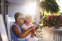 Девушка и бабушка играют в смартфоны на крыльце на закате — стоковое фото