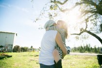 Mid adult woman and daughter hugging in sunlit park — Stock Photo