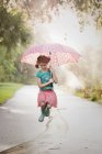 Girl holding up umbrella and jumping puddles on street — Stock Photo