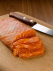Нарезанный лосось и нож на доске — стоковое фото