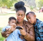 Mère et enfants assis textos sur smartphone regardant vers le bas — Photo de stock