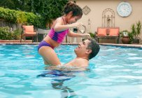 Seitenansicht des Vaters, der Mädchen im Schwimmbad hochhebt, von Angesicht zu Angesicht lächelnd — Stockfoto