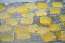 Ravioles amarillos con harina sobre mesa gris - foto de stock