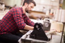 Мужчина ткач с помощью швейной машины на старой текстильной фабрике — стоковое фото
