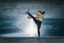 Young woman, working out, doing high kick, outdoors, at night — Stock Photo