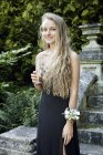 Adolescente portant une robe de bal et un corsage tenant une flûte à champagne regardant la caméra sourire — Photo de stock