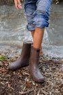 Chica quitándose las botas de lluvia por estanque, tiro recortado - foto de stock