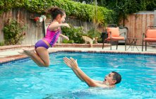 Vista lateral del padre atrapando chica saltando en la piscina, en el aire - foto de stock