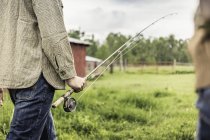 Cropped view of young mans mid section carrying fishing rod — Stock Photo
