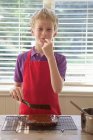 Boy tasting cake frosting in kitchen — Stock Photo