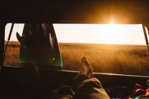 Male surfer with bare feet up in back of jeep at sunset, San Luis Obispo, California, USA — Stock Photo