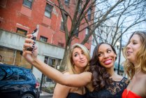 Tres glamorosas amigas adultas jóvenes tomando selfie de teléfonos inteligentes en la calle - foto de stock