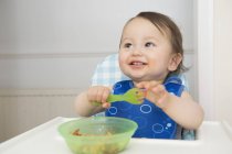 Baby boy eating baby food in kitchen high chair — Stock Photo