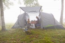 Mãe e filhos tomando café da manhã na tenda na paisagem nebulosa — Fotografia de Stock