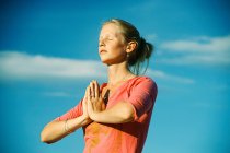 Mujer meditando bajo el cielo azul - foto de stock