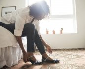 Reife Frau sitzt auf Bett und zieht Schuhe an — Stockfoto