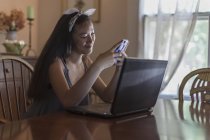 Девочка-подросток работает дома на ноутбуке и смартфоне в столовой — стоковое фото