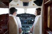 Visão traseira de pilotos masculinos e femininos falando no cockpit do jato particular — Fotografia de Stock