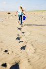 Visão traseira da menina correndo pela areia na praia — Fotografia de Stock