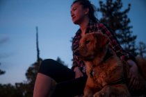 Visão de baixo ângulo da jovem mulher sentada com o braço ao redor do cão olhando para longe — Fotografia de Stock