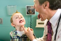 Médico masculino olhando para a língua do menino — Fotografia de Stock