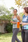 Jovens mulheres andando usando roupas esportivas carregando garrafas de água rindo — Fotografia de Stock