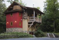 Будинок в стилі котеджу з кам'яним, червоним вертикальним дерев'яним сайдингом і дерев'яним балконом в сутінках влітку — стокове фото