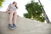 Молода жінка сидить на стіні дивиться скейтбордист — стокове фото