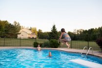 Молодая девушка прыгает в бассейн, отец и бабушка смотрят — стоковое фото