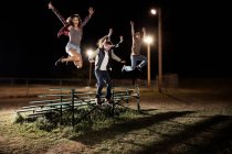 Quatro amigos saltando sobre bancadas à noite — Fotografia de Stock
