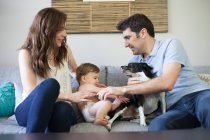 Family with baby boy sitting on sofa playing with dog — Stock Photo