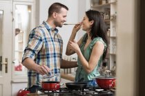 Mid adult couple cooking dinner, tasting — Stock Photo