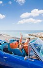 Man and woman in car by sea waving — Stock Photo