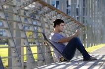 Young man sitting, using mobile phone, skateboard beside — Stock Photo