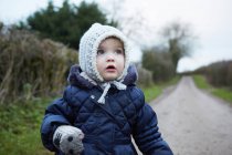 Portrait of female toddler in knit hat and gloves on rural road — Stock Photo