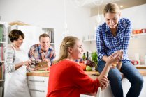 Zwei Frauen mit Handy in der Küche, Mutter und Bruder im Hintergrund — Stockfoto