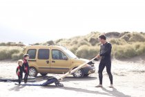Padre con dos hijos, tabla de surf y coche en la playa - foto de stock
