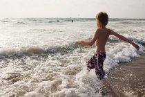 Junge läuft in Wellen am Strand — Stockfoto