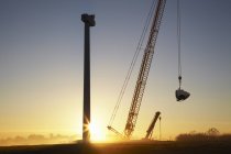 Erecting wind turbine and crane silhouettes on sunset sky — Stock Photo