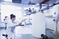Giovane scienziata che contempla note di ricerca sul banco da lavoro del laboratorio — Foto stock