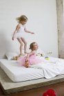 Two little sisters dressed as ballet dancers playing on bed — Stock Photo