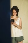 Молодая женщина, прислонившись к стене, читает текст на смартфоне — стоковое фото