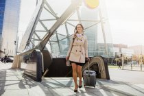 Бізнес-леді з колісною валізою від ескалатора — стокове фото
