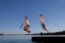 Padre e hijo saltando al lago - foto de stock